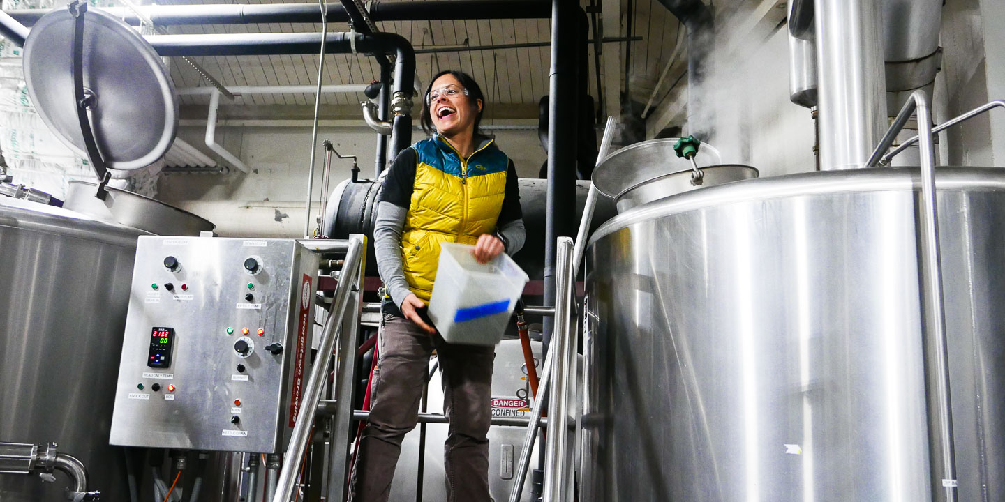 Brewer Tina laughs while adding hops to the boil kettle