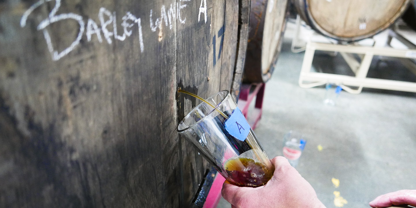 Brewer Chad takes a sample of barleywine from a barrel for testing