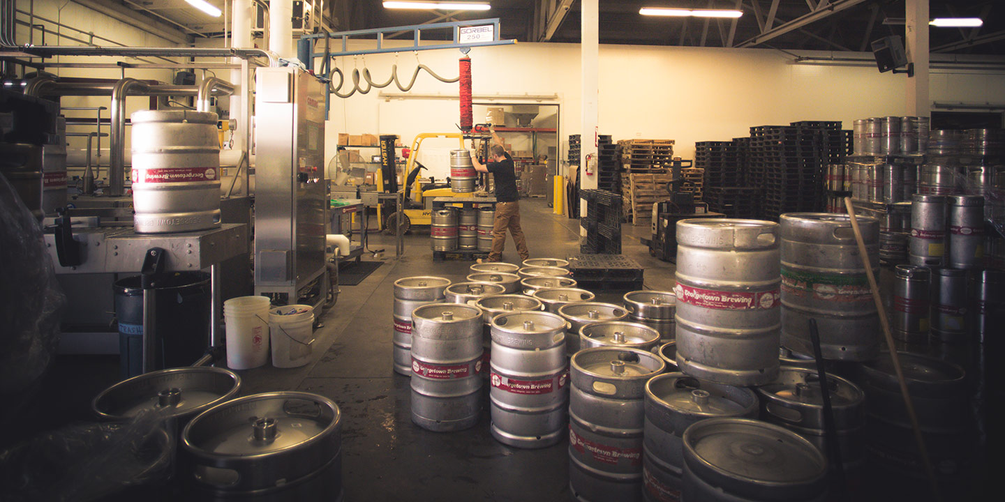 a single brewer working on the keg filler, surrounded by empty kegs