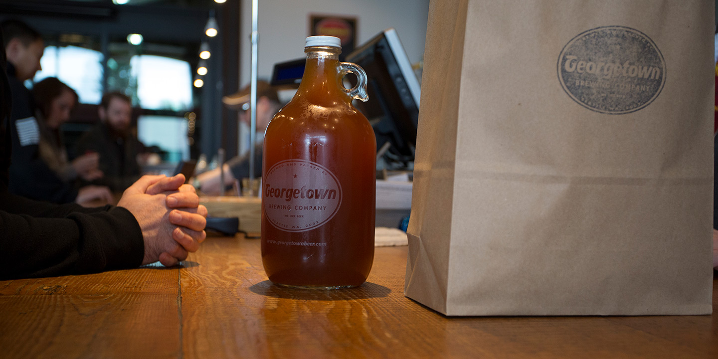 growler on the counter being handed off to a customer along with a bag of shirts purchased